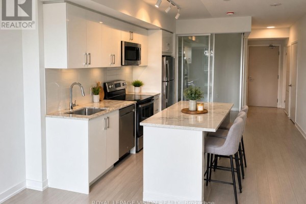 View of the kitchen with white cabinets, island seating, and access to a glass-partitioned room. - 329 - 4010 Eglinton Avenue W, Toronto