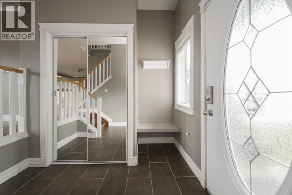Foyer with dark tile flooring, a mirrored closet, a bench, and a white oval glass front door. - 329 Archibald Close, Fort Mcmurray