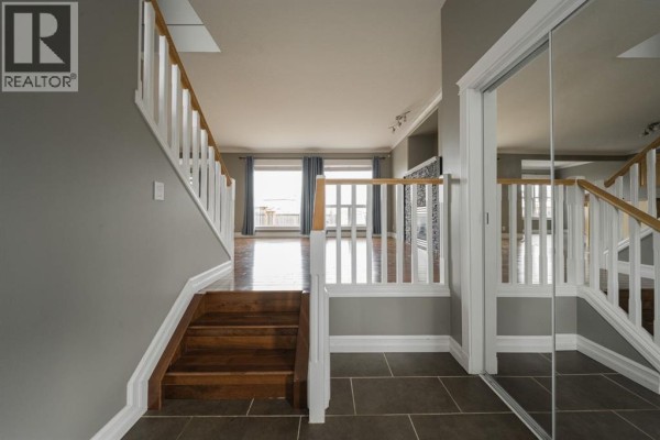 Interior view of a foyer with a staircase, wood flooring, and large windows with blue curtains. - 329 Archibald Close, Fort Mcmurray