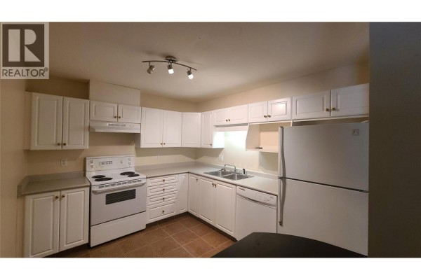 White kitchen cabinets with brass hardware, white stove, and grey countertops. - 329 Rigsby Street Unit# 102, Penticton
