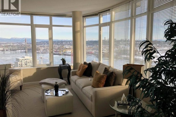 Living room with large windows offering city and water views, beige carpet, and light-colored sofa. - 32xx 888 Carnarvon St, New Westminster