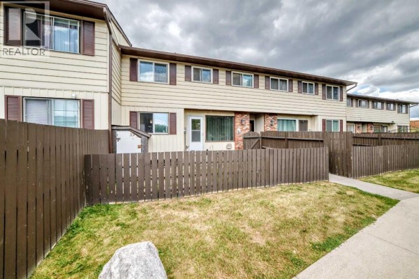 Side view of the townhouse complex showing multiple units and a wooden fence. - 33, 175 Manora Place, Calgary