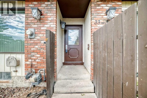 Close-up of the townhouse entrance with brick accents and a wooden fence. - 33, 175 Manora Place, Calgary