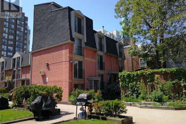 Rear view of pink brick townhouses with gardens, patios, and a barbecue. - 33 - 325 Jarvis Street, Toronto