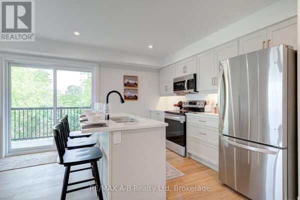 Modern kitchen with light gray cabinets, stainless steel appliances, and island seating. - 33 - 428 Queen Street W, St  Marys
