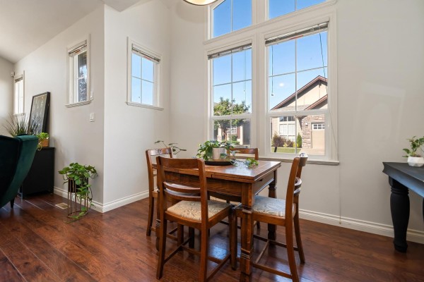 Dining area with a wooden table, chairs, and large windows overlooking a residential street. - 33 6577 Southdowne Place, Sardis South, Chilliwack