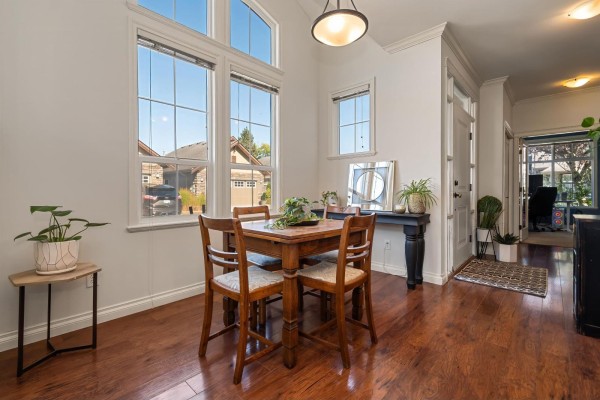 Dining area with a wooden table, chairs, and large windows; doorway to backyard visible. - 33 6577 Southdowne Place, Sardis South, Chilliwack