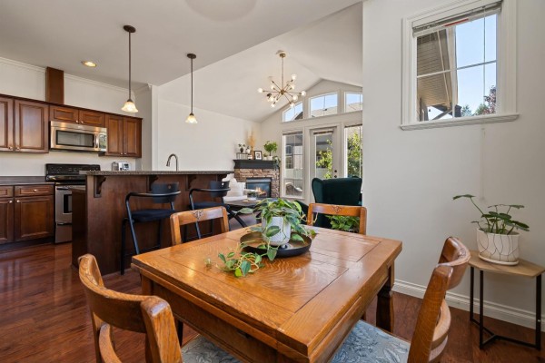 Kitchen with dark wood cabinets, granite countertops, island with stools, and adjoining living area. - 33 6577 Southdowne Place, Sardis South, Chilliwack