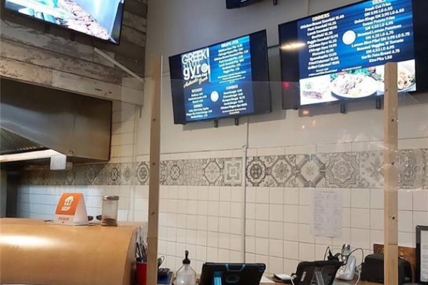 Restaurant counter with plexiglass barrier, digital menus displaying food items, and a tablet. - 33 Ainslie Street, Cambridge