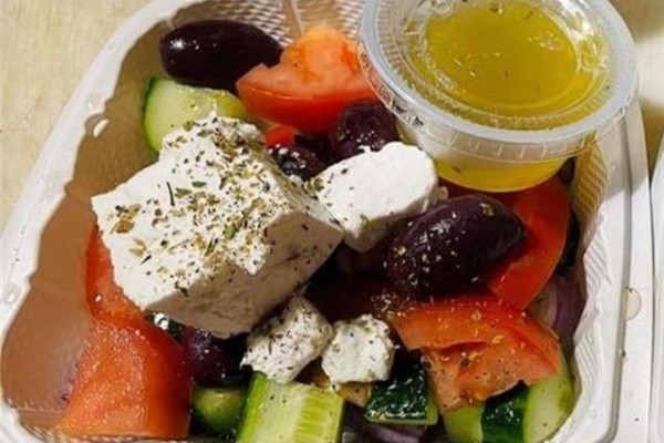 Close-up of a Greek salad in a white takeout container with feta, olives, and tomatoes. - 33 Ainslie Street, Cambridge