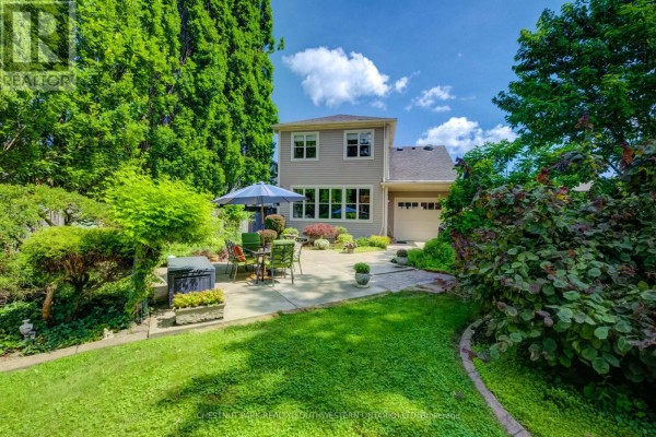 Backyard view of a house with a patio, lawn, garden beds, trees, and a detached garage. - 33 Cherry Street, St  Catharines