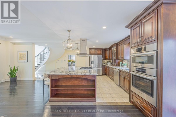 Kitchen with island, stainless steel appliances, and curved staircase - 33 Deerford Road Toronto