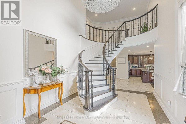 Interior foyer with a grand curved staircase, marble floors, and a console table. - 33 Deerford Road, Toronto