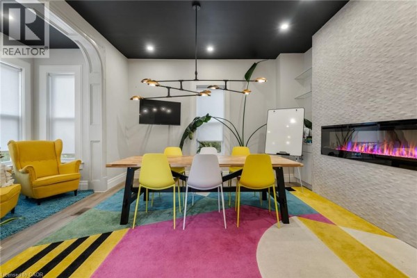 Meeting room with yellow accent chairs, modern light fixture, electric fireplace, and view of the adjacent office space. - 33 E Young Street E, Waterloo