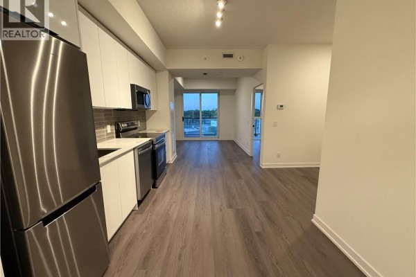 Open-concept living area with a modern kitchen, gray flooring, and balcony access. - 33 Erie Avenue Unit# 506, Brantford