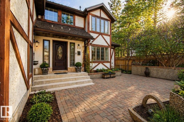 Front exterior of a house with a paved walkway, stone steps, and lush greenery. - 33 Glen Meadow Cr, St  Albert