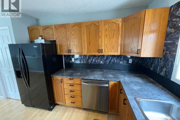 Kitchen with light wood cabinets, black refrigerator, stainless steel dishwasher, and dark countertops. - 33 Graham Road, Whitecourt