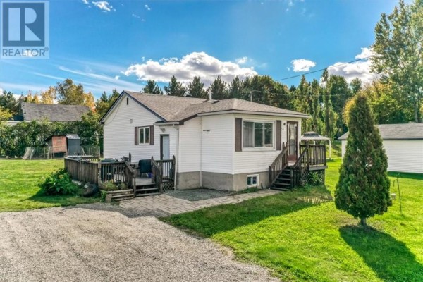Rear and side view of a white bungalow, featuring a wooden deck, gravel driveway, and storage shed. - 33 Graham Road, Whitefish