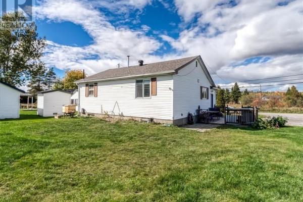 Side and rear view of a white house with a lawn, trees, and a shed in the background. - 33 Graham Road, Whitefish