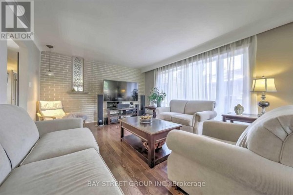 Living room with hardwood floors, seating, coffee table, television, and a brick accent wall. - 33 Heathview Avenue, Toronto