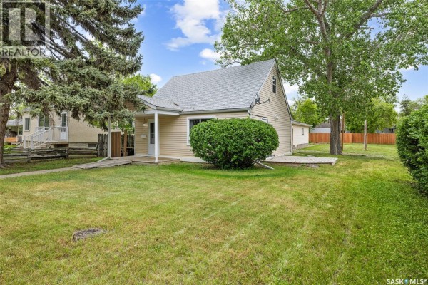 Exterior view of a light yellow house with a sloped roof and green lawn. - 33 Merritt Crescent, Regina