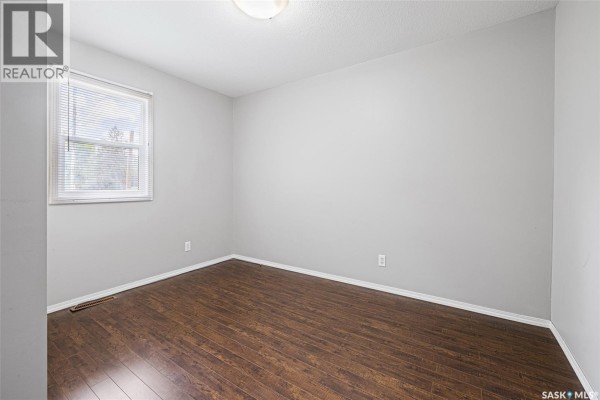 Empty bedroom with dark wood floors and light grey walls with a single window. - 33 Merritt Crescent, Regina