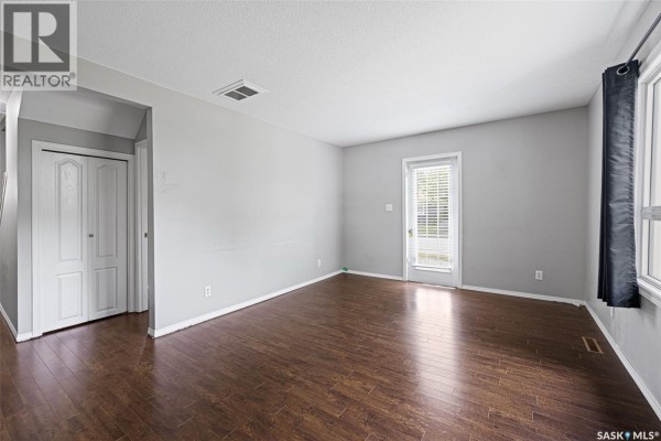 Living room showing entry closet doors, dark wood floors, and a back door. - 33 Merritt Crescent, Regina