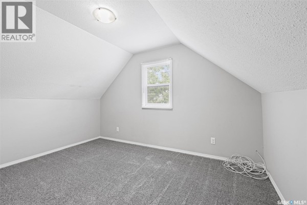Attic bedroom with sloped ceilings, grey carpet, and a single window. - 33 Merritt Crescent, Regina