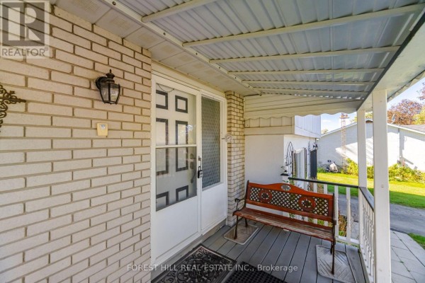 Close-up of a covered front porch with a white door, brick siding, and a wooden bench. - 33 Rice Drive, King