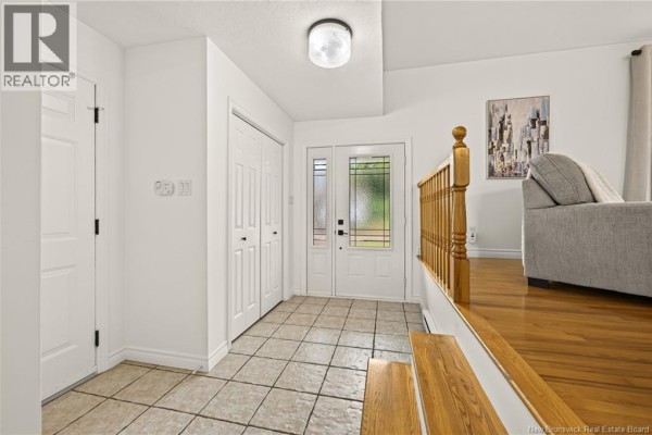 Tiled entryway with double closet, glass-paned front door, and wooden banister. - 33 Robichaud Court, Dieppe