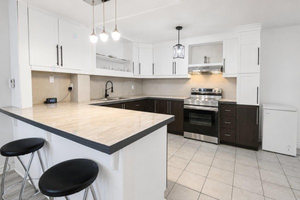Kitchen island with two black stools, dark wood lower cabinets, and stainless steel appliances. - 33 Rue De Dubuc, Gatineau