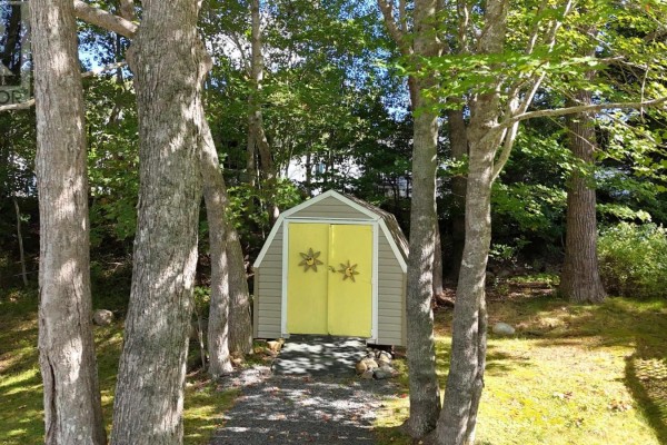 A small, grey garden shed with bright yellow double doors is nestled amongst trees. - 33 Spring Crescent, Bridgewater