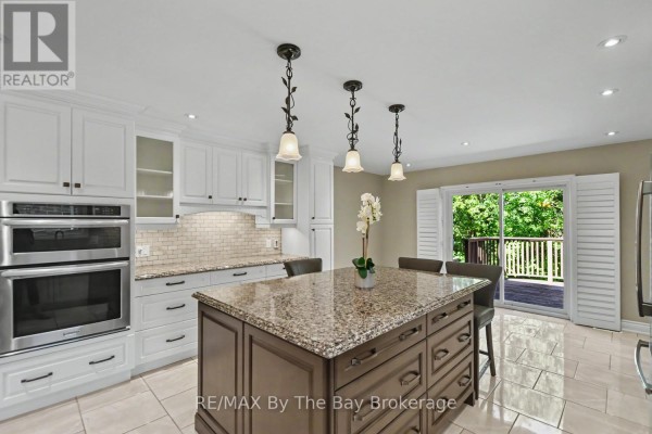 Kitchen with white cabinets, granite island, stainless steel double ovens, and deck access. - 33 Telfer Road, Collingwood