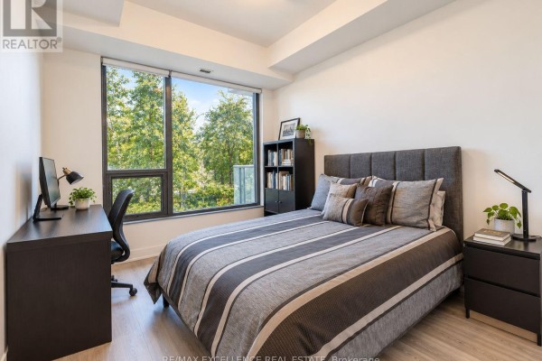 Bedroom with a queen-sized bed, a desk, and a large window overlooking trees. - 330 - 280 Howland Avenue, Toronto