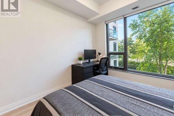 Bedroom with a bed, desk, and a large window showing an adjacent building and trees. - 330 - 280 Howland Avenue, Toronto