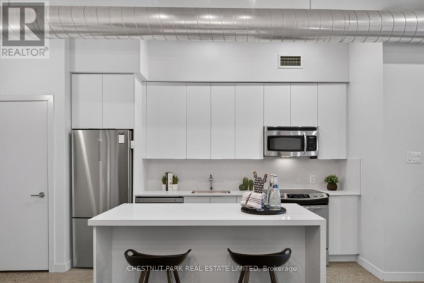 Modern kitchen with white cabinetry, stainless steel appliances, and a large island with stools. - 330 - 510 King Street E, Toronto