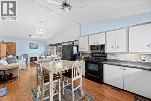 Open-concept living area and kitchen with a dining table, fireplace, and white cabinets. - 330 6 Street, Salmon Arm