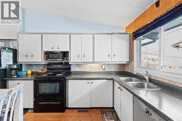 Kitchen with white cabinets, black appliances, and a double sink overlooking the yard. - 330 6 Street, Salmon Arm