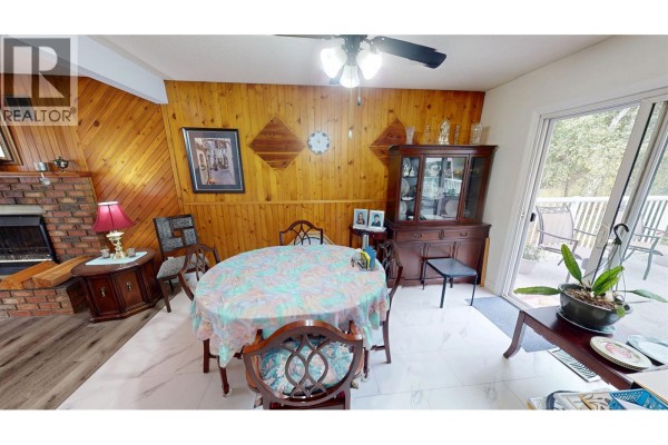 Dining area with a round table, wood-paneled walls, and a brick fireplace. - 330 Caragana Road, Quesnel