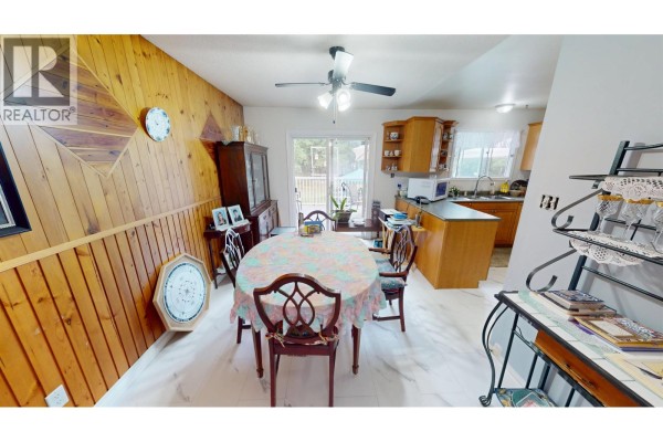 Dining area with wood paneling, a sliding glass door to a deck, and a view of the kitchen. - 330 Caragana Road, Quesnel