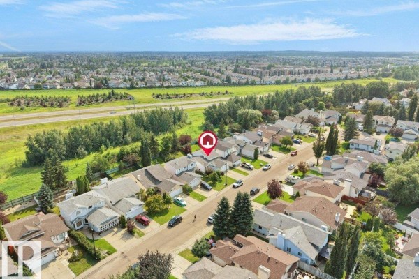 Aerial perspective of a residential street lined with houses, surrounded by green spaces and a highway. - 330 Pearson Cr Nw, Edmonton
