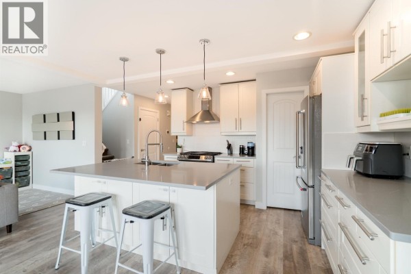 Spacious white kitchen with a large island, stainless steel appliances, and stairs leading to another level. - 330 Richmond Street, New Westminster