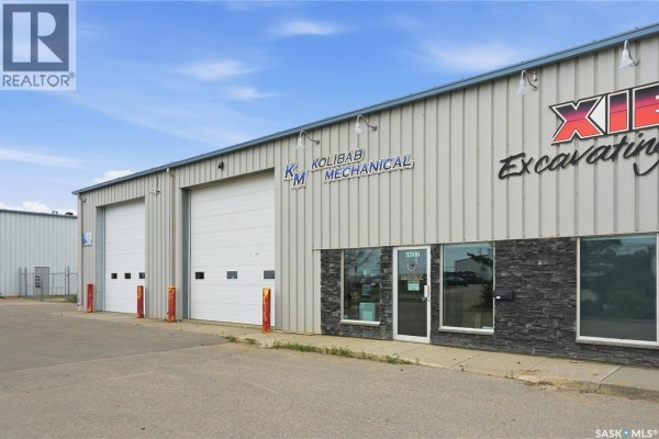 Close-up of the commercial building's front, featuring two large white bay doors and an entranceway with dark stone accents. - 3302 Faithfull Avenue, Saskatoon