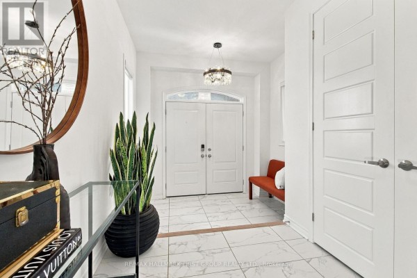 A bright, white foyer with a chandelier, double doors, and a snake plant in a black pot. - 3302 Marchington Square, Pickering