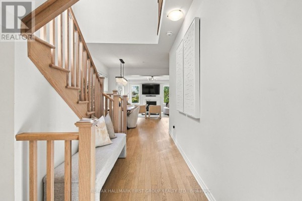 View down a hallway with a light wood staircase and bench, leading to a living room with a fireplace. - 3302 Marchington Square, Pickering