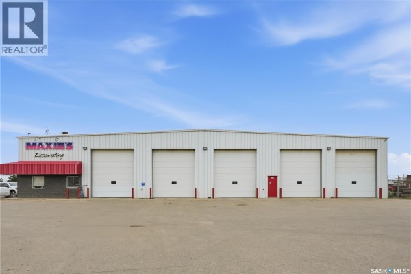 Commercial building exterior with five white garage doors and one red door under a bright blue sky. - 3303 Faithfull Avenue, Saskatoon