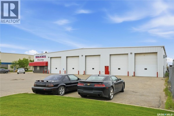 Two black cars parked on grass in front of a commercial building with white garage doors. - 3303 Faithfull Avenue, Saskatoon