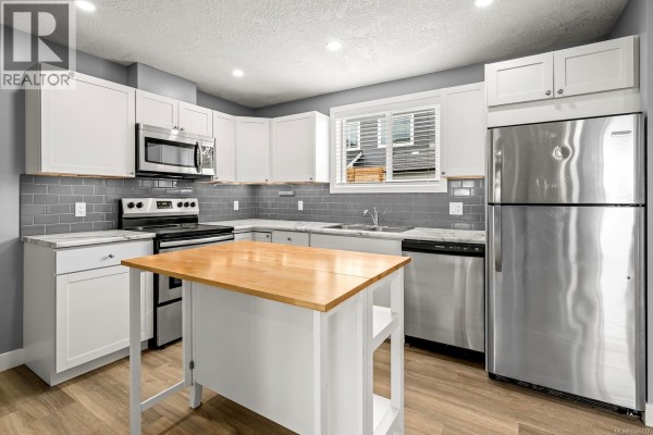 Kitchen with white cabinets, stainless steel appliances, and a wooden island with two bar stools. - 3303 Seventh St, Cumberland