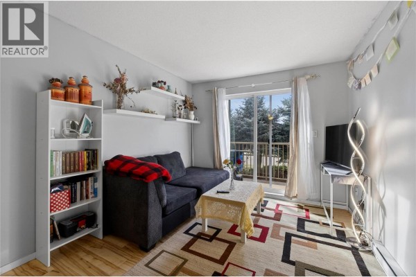 Living room with a dark sofa, patterned rug, and access to a balcony. - 3304 35th Avenue Unit# 215, Vernon