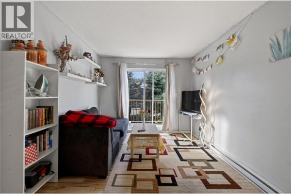 Living room featuring a dark sofa, decorative shelves, and a television. - 3304 35th Avenue Unit# 215, Vernon